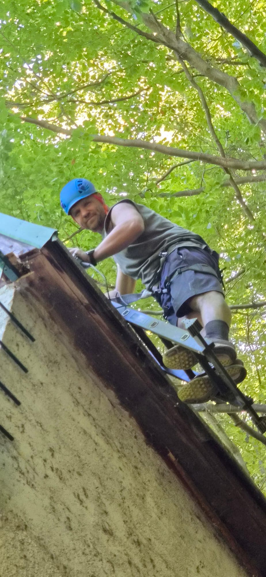 Ivan na rebríku na streche chaty v prilbe, okolo bukový les