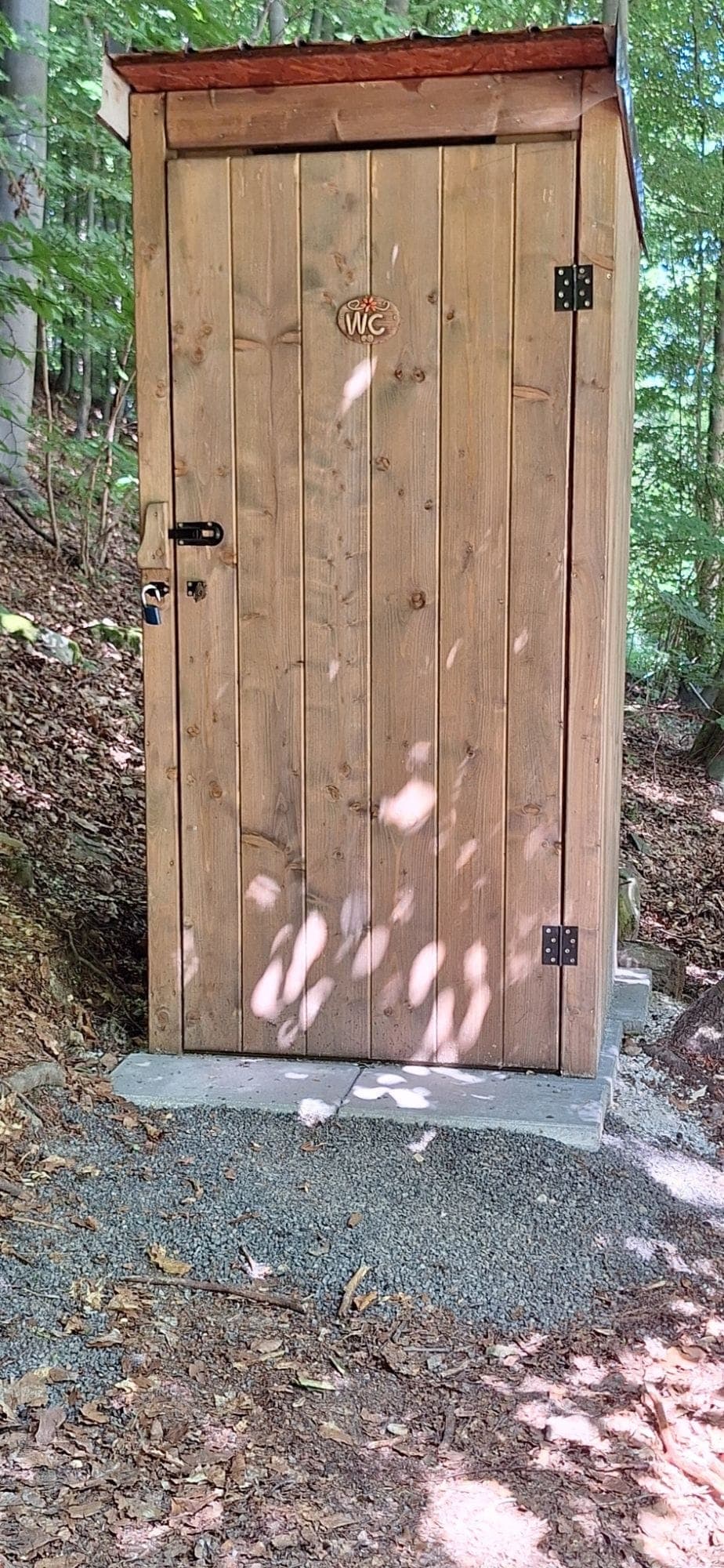 Nové drevené suché WC s tabuľkou WC na dverách, na štrkovom podklade v lese