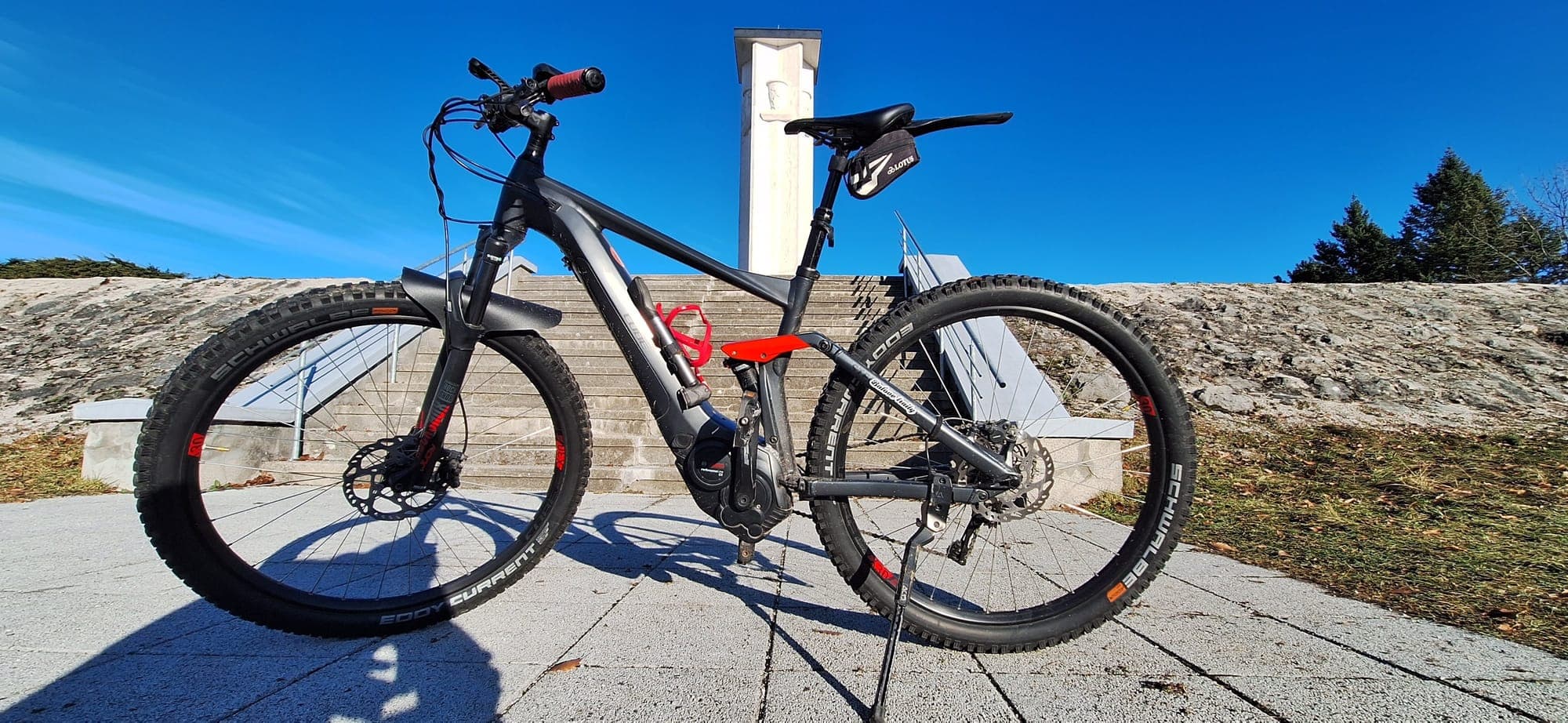 Horský bicykel opretý na kamennej vyhliadke pod modrou oblohou