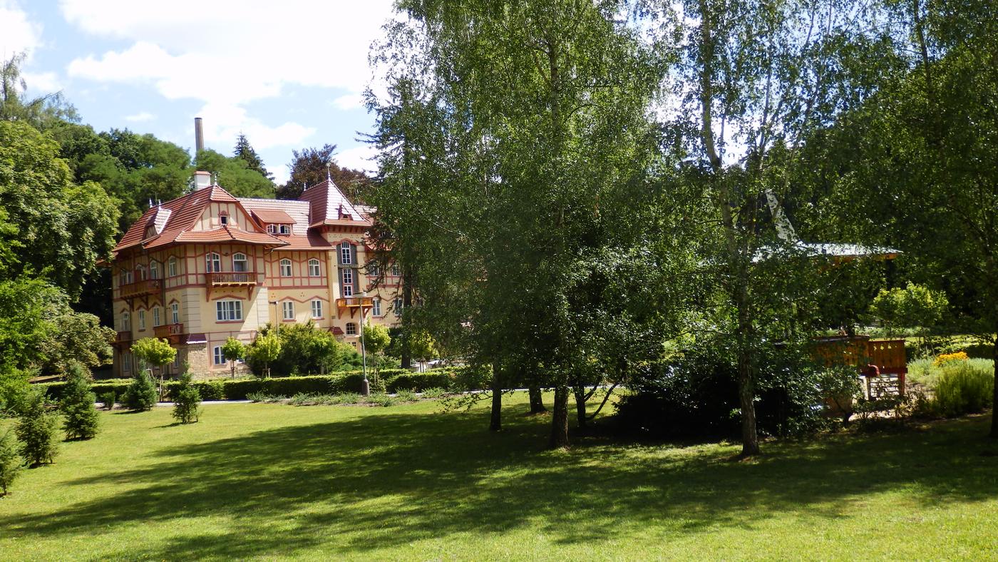 Vila s červenou strechou za stromami kúpeľného parku